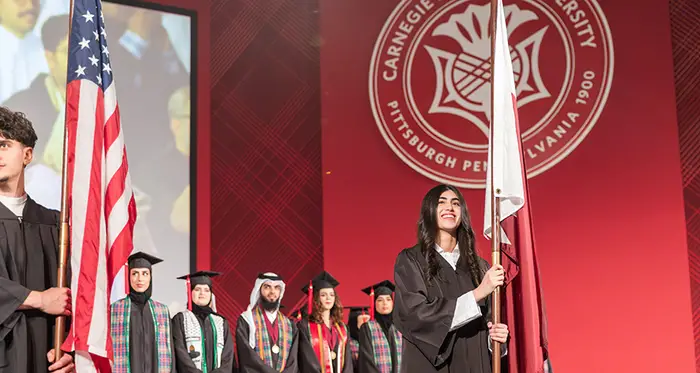 Students hold flags on stage at the CMU-Q graduation ceremony.