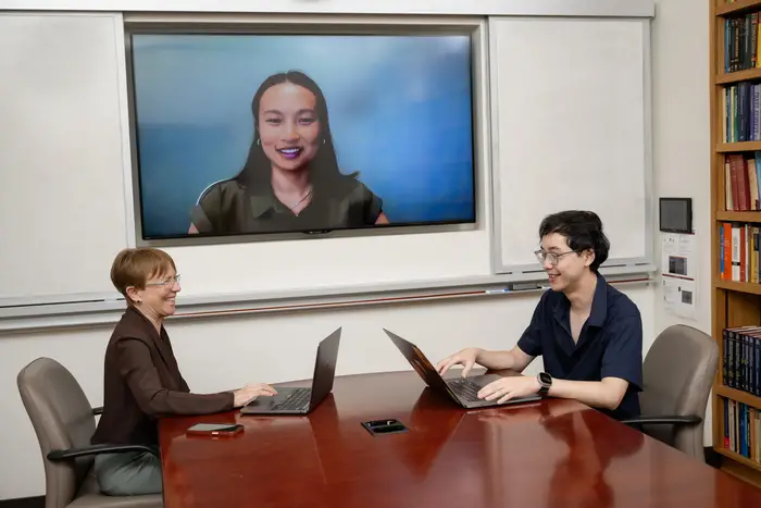 Kathryn Roeder and Jin-Hong Du seated at a table with Maya Shen appearing on a screen.