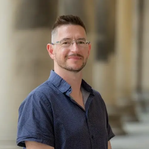 A man with close cropped brown hair wearing glasses and a blue collared shirt
