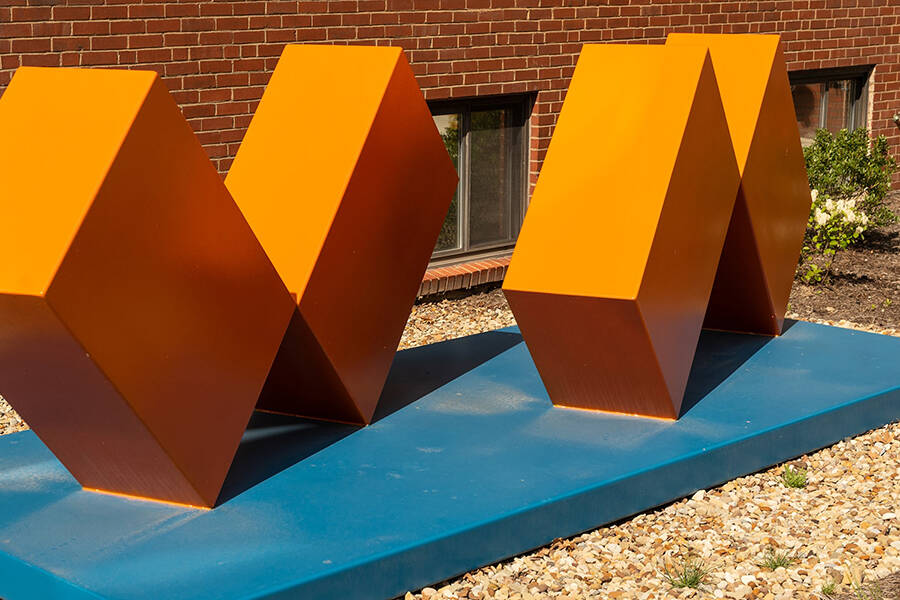 boxy orange steel sculpture on blue base outdoors