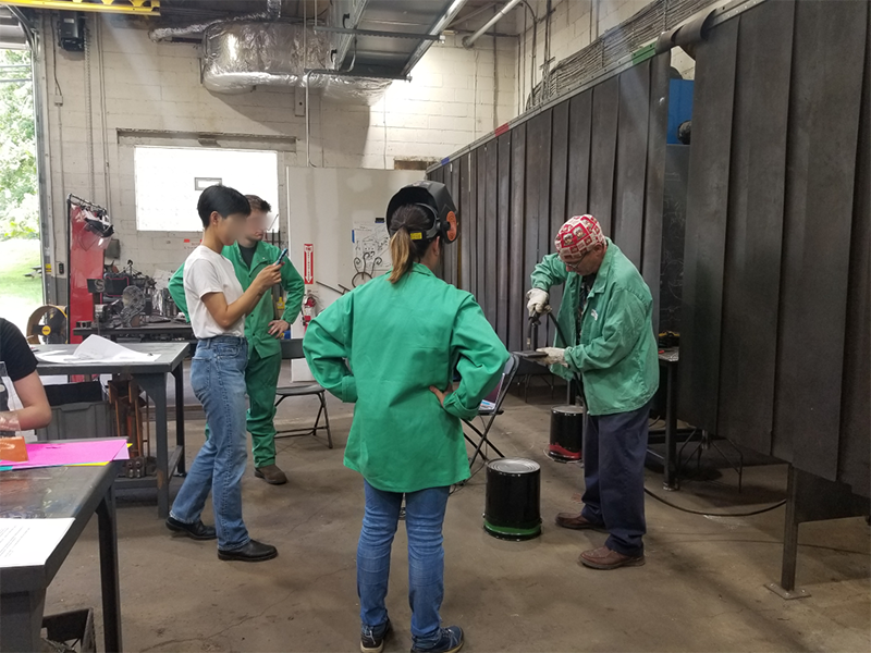 Photo of a welding instructor demonstrating proper technique to students
