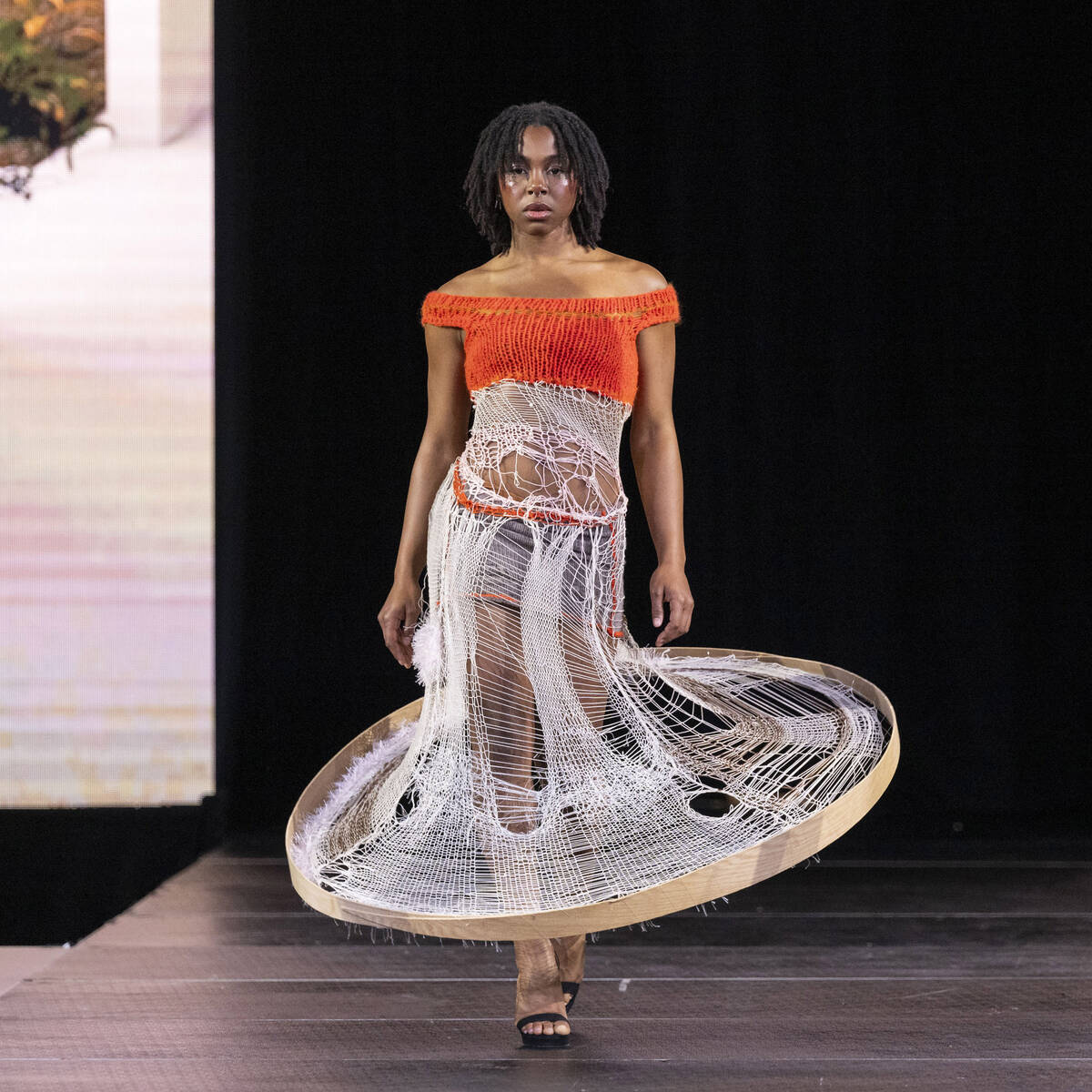 Model wearing orange knit top and distressed white knit hoop skirt.