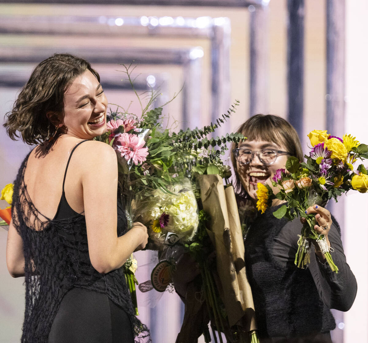 Two designers smile onstage with flowers.