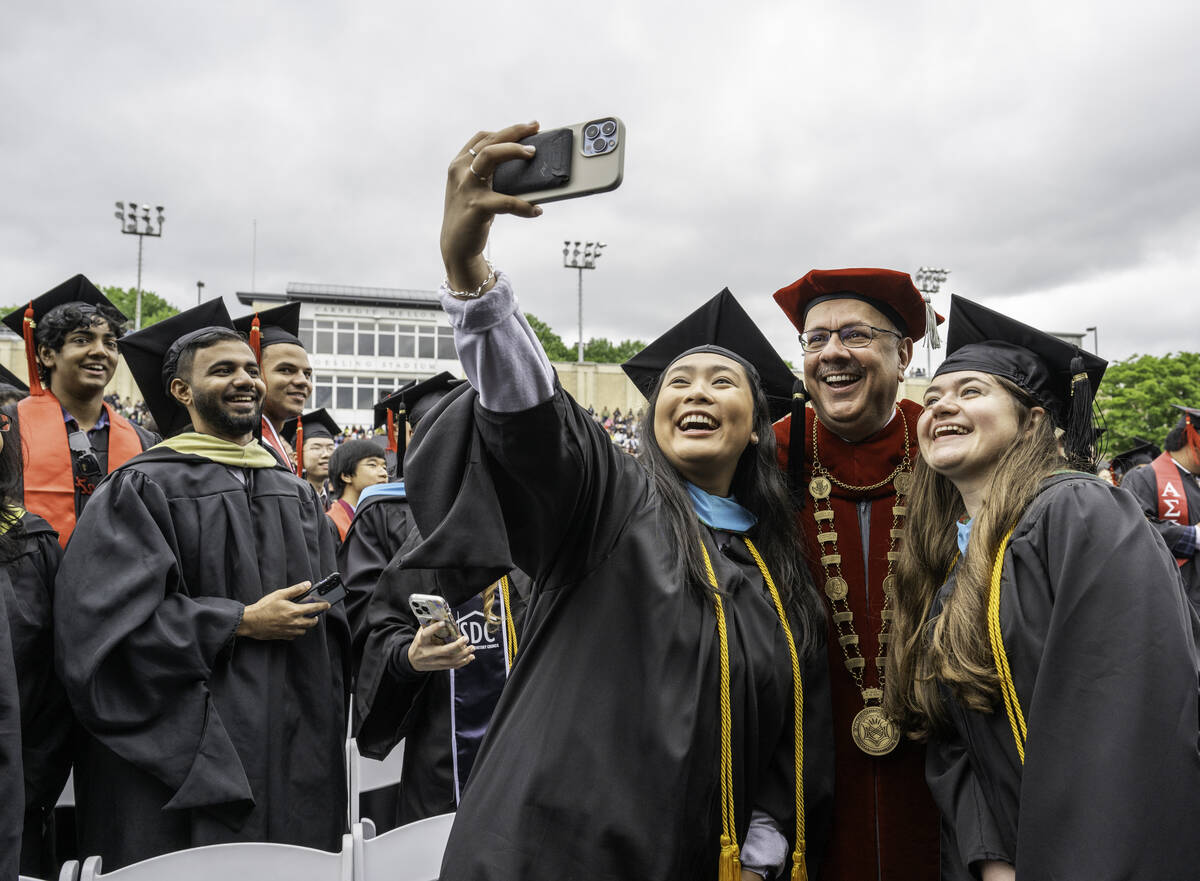 Farnam Jahanian takes a photograph with students at Commencement. 