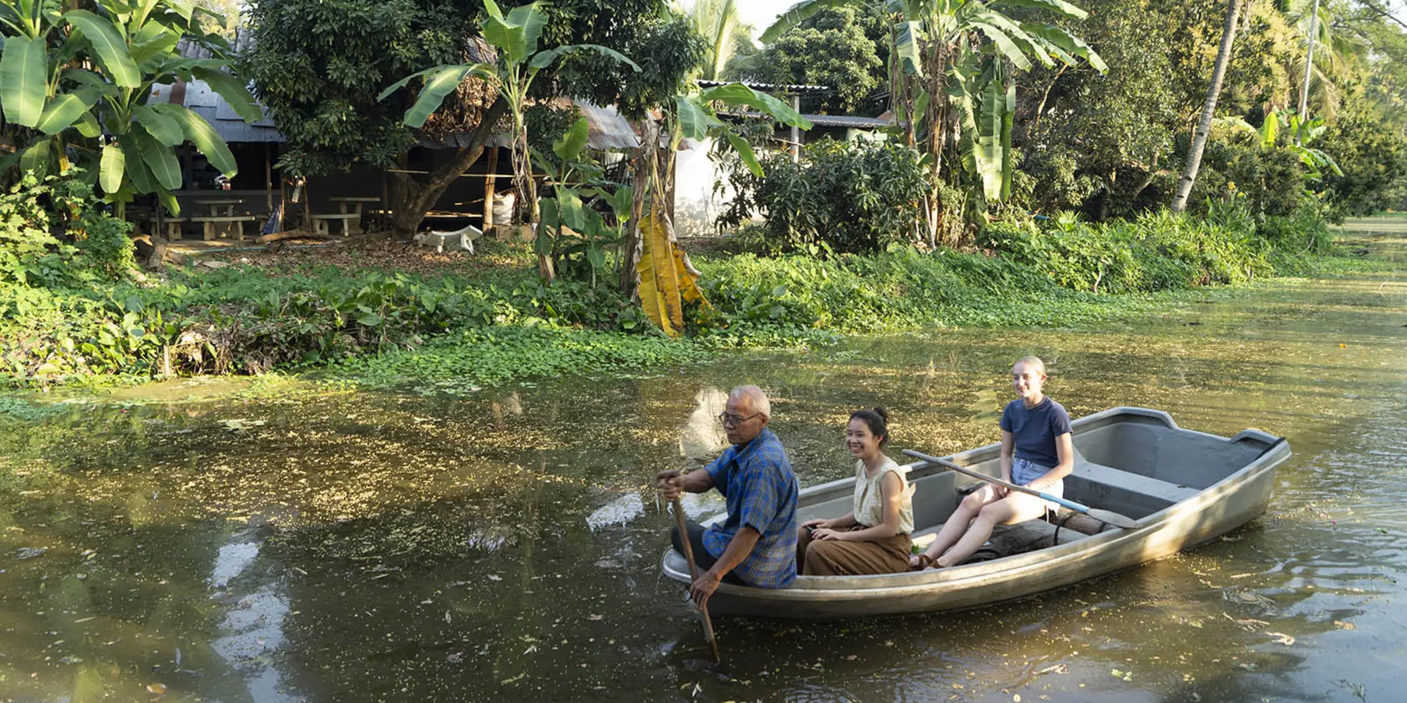three people in boat on canal passing village