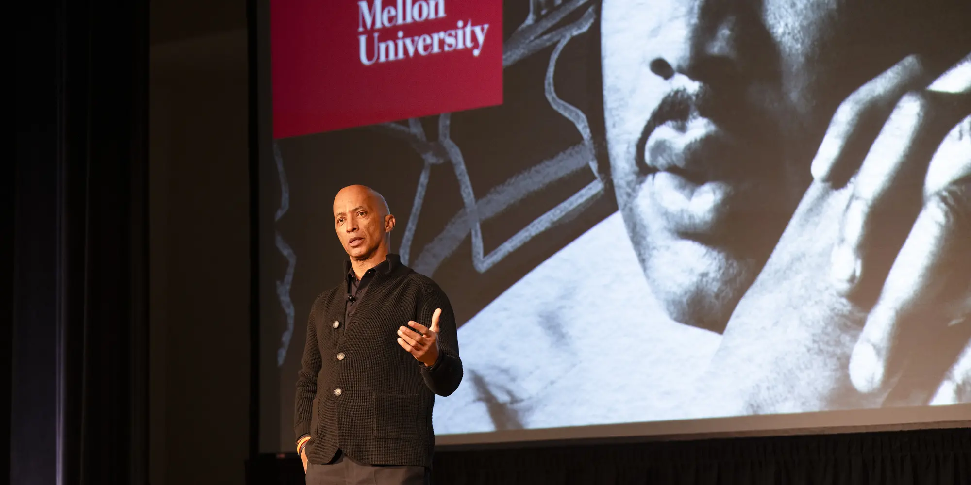 Byron Pitts on stage in front of big screen displaying image of MLK and CMU logo