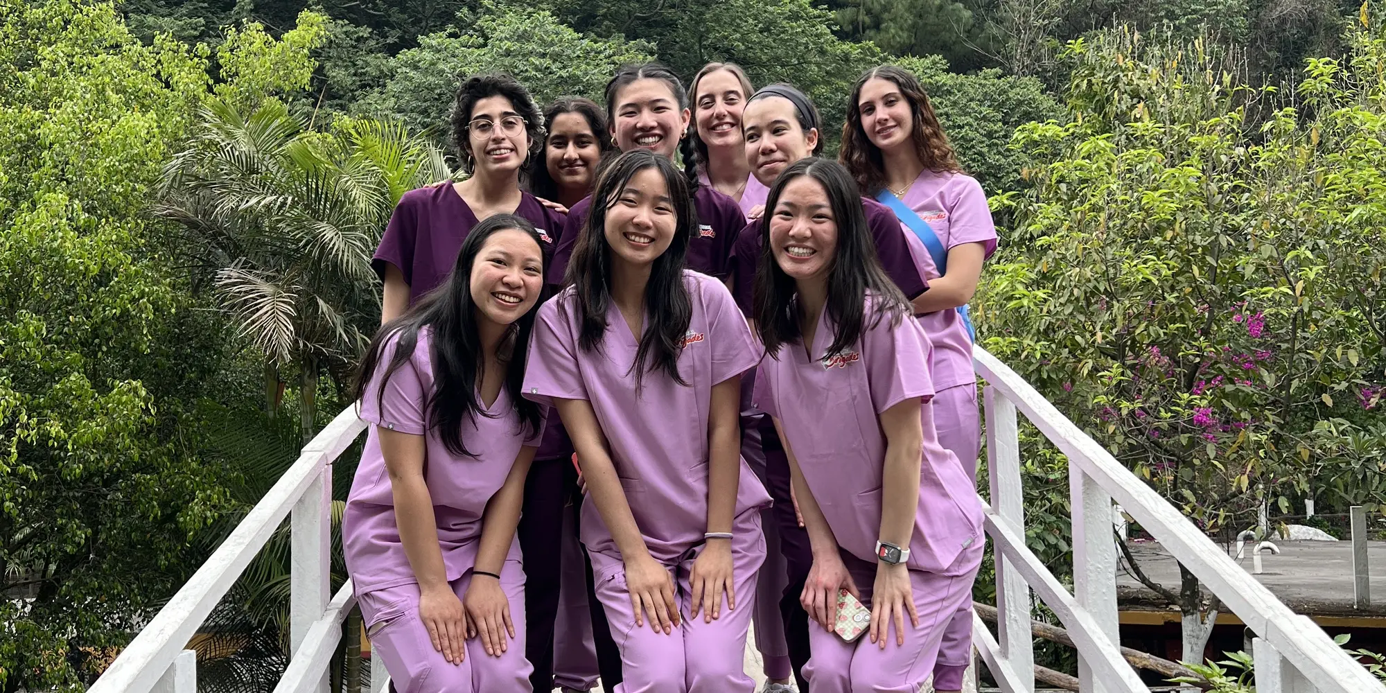 Small group of students wearing scrubs posing outdoors with trees in background