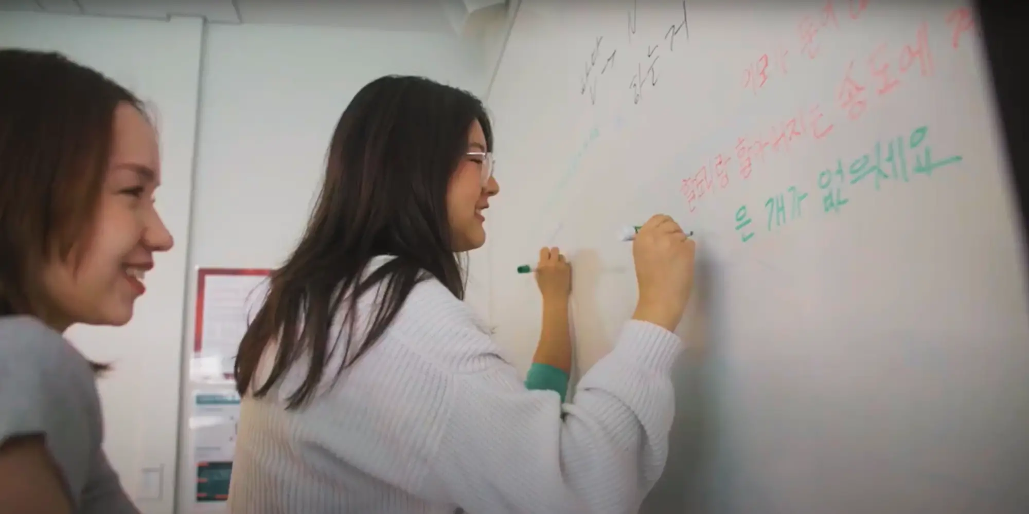 Students writing in Korean on a whiteboard.