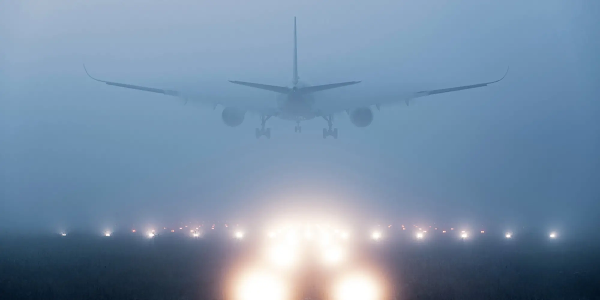 An airplane landing on a runway in heavy fog. The lights along the runway are blurry through the fog.