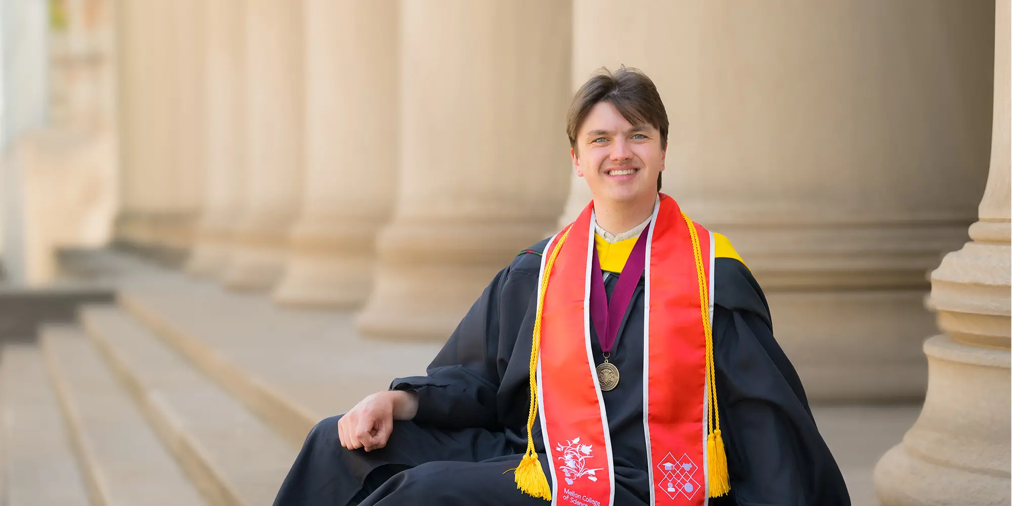graduate in gown seated on steps of Mellon Institute