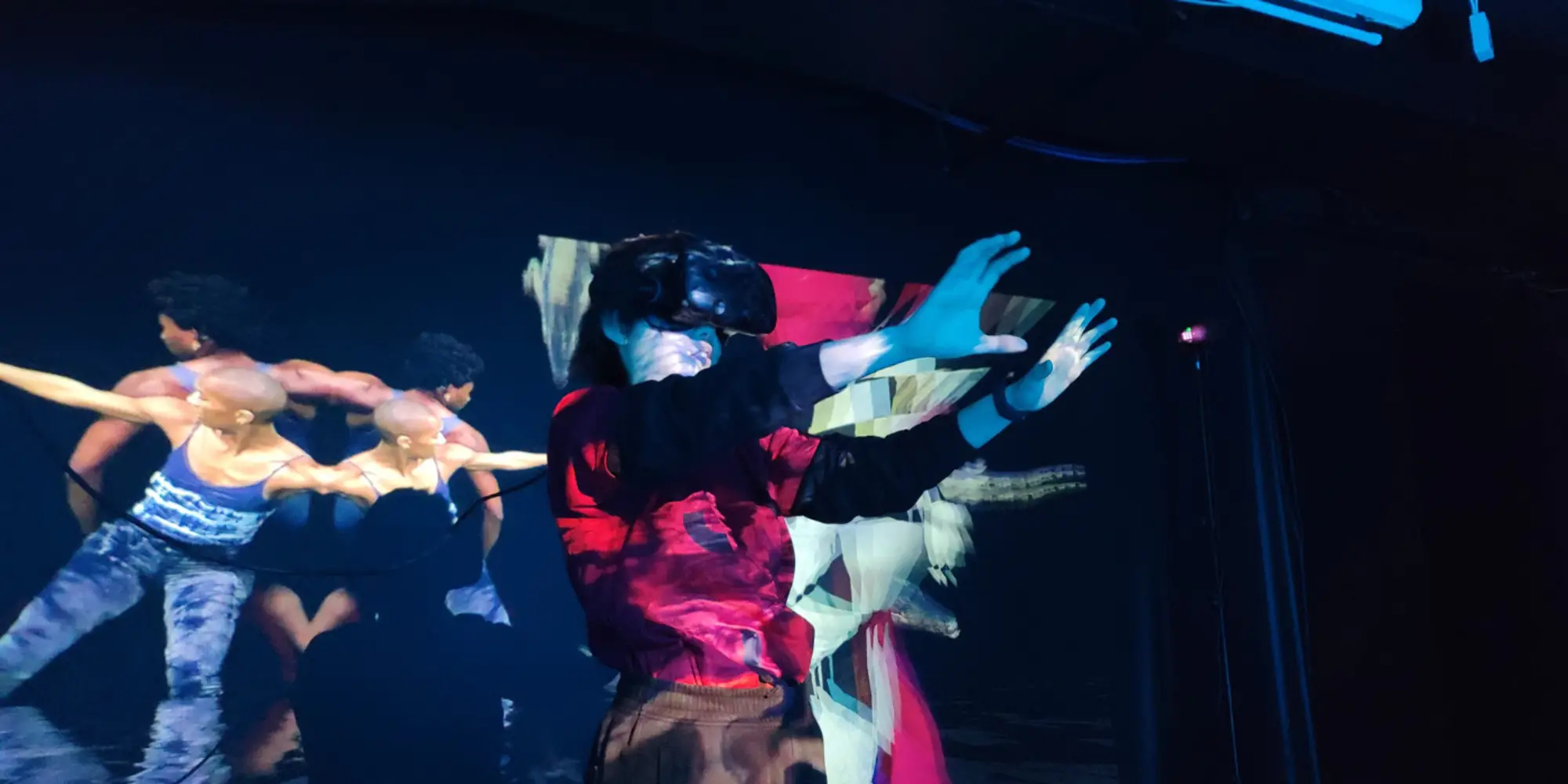 Person wearing virtual reality goggles while a video of dancers plays behind them
