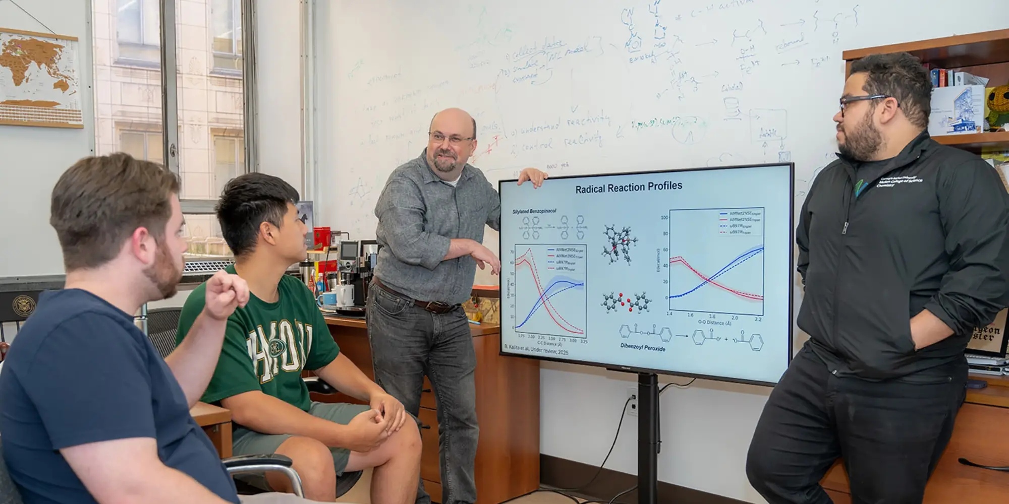Olexandr Isayev and Gabe Gomes stand next to a screen as they talk to Robert MacKnight and Nick Gao