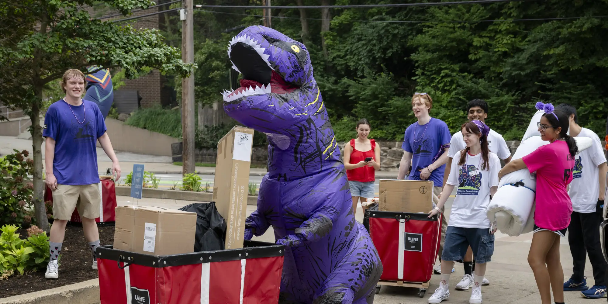 A person in a purple inflatable dinosaur costume helps move students into CMU. 