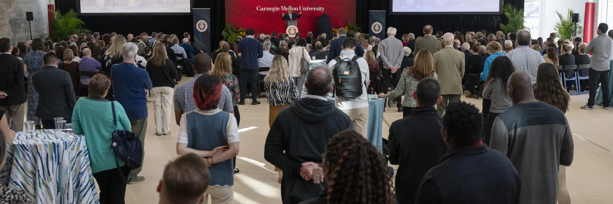 People gather in a gymnasium in front of a stage.