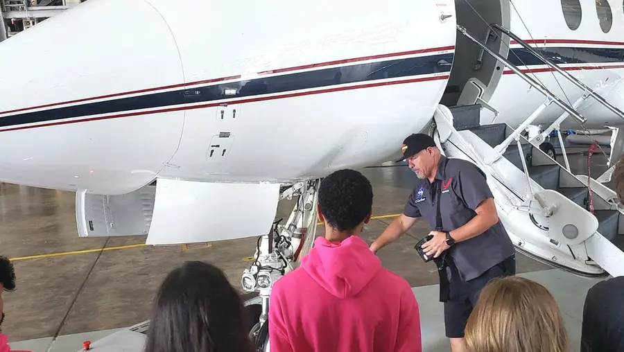 People standing in front of an airplane in a hangar on the ground.