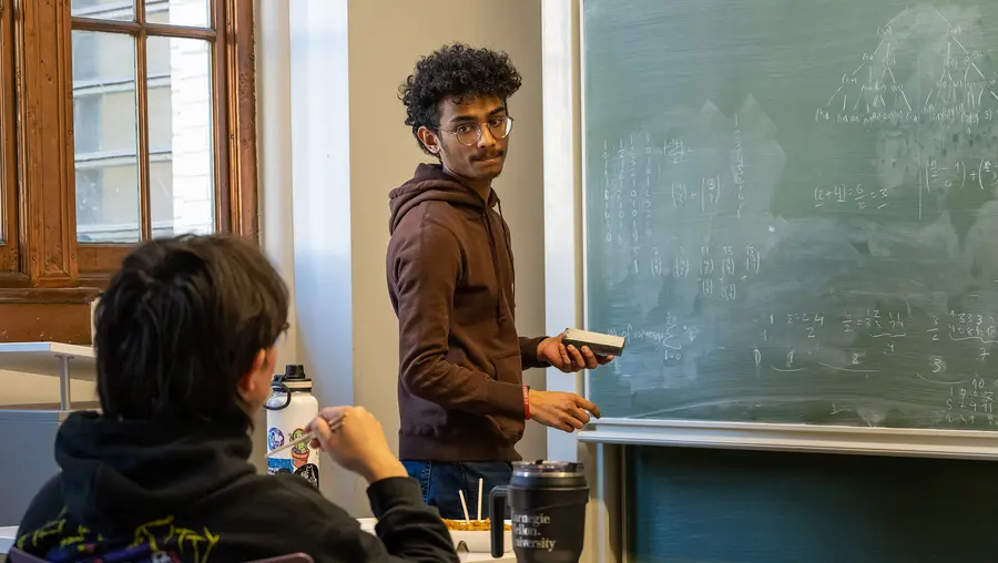 student at chalk board and student seated trying to solve a math problem