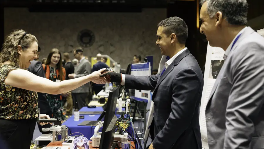 A Congressional staffer shakes the hand of a researcher wearing a special glove that controls a robot