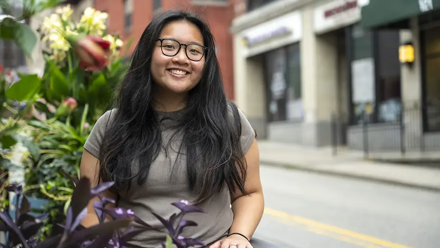 Girl smiling on street near flowers with shops in background