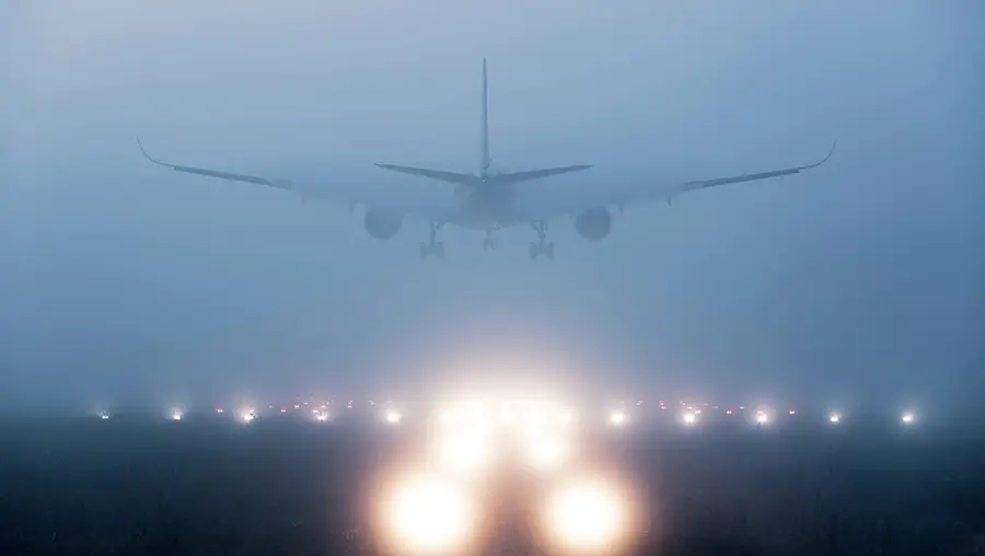 An airplane landing on a runway in heavy fog. The lights along the runway are blurry through the fog.