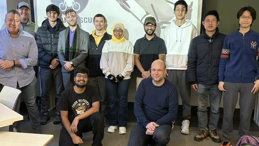 A group photo of people in front of a projector screen showing a drone. 