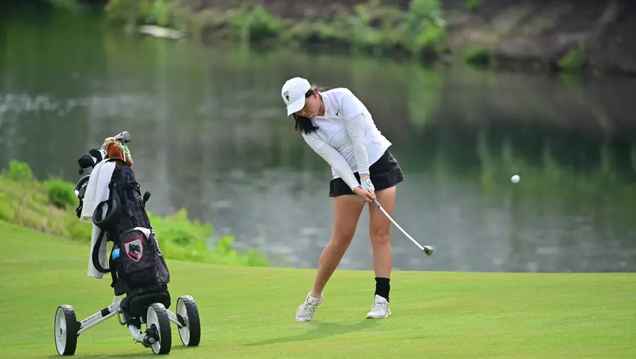 A golfer hits a ball next to a lake.