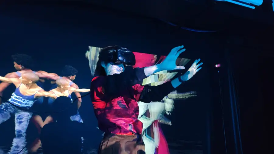 Person wearing virtual reality goggles while a video of dancers plays behind them