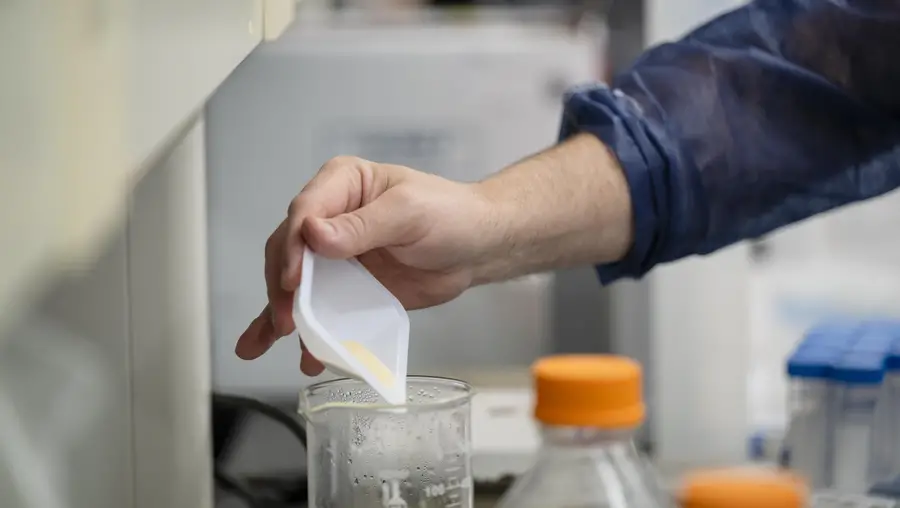 photos shows a hand using a white tray to add powder to a beaker