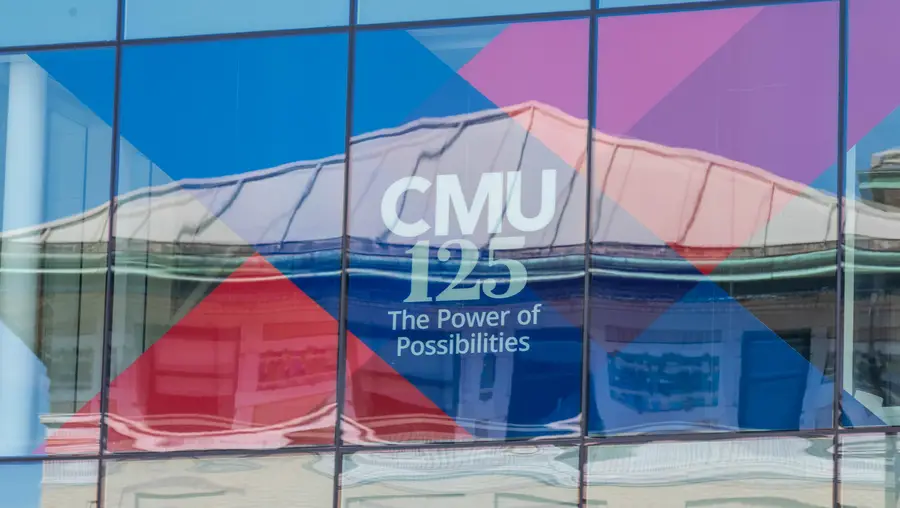 A picture of a window reflecting a building. In the window is a red and blue banner for CMU's 125th celebration. 