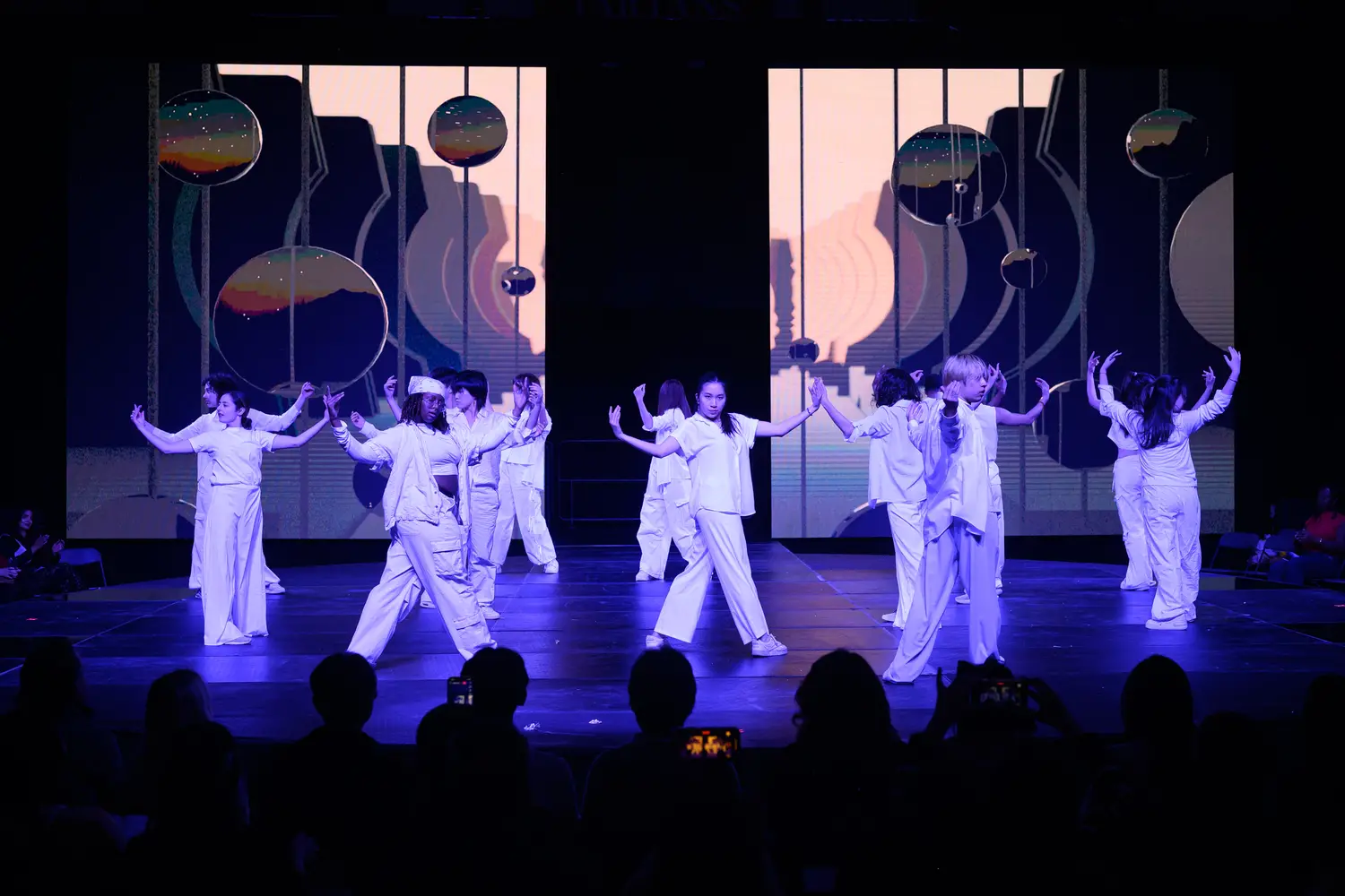 Dancers dressed in white hold their arms outstretched to the side, turning to face the audience