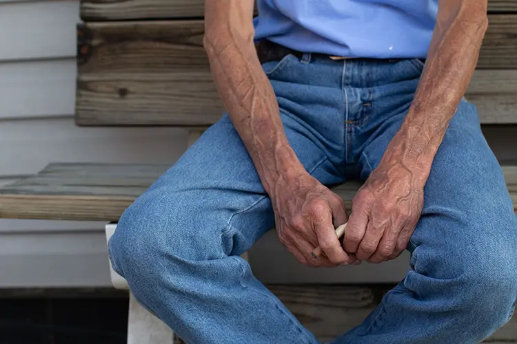 partial shot of man sitting on bench holding cigarette