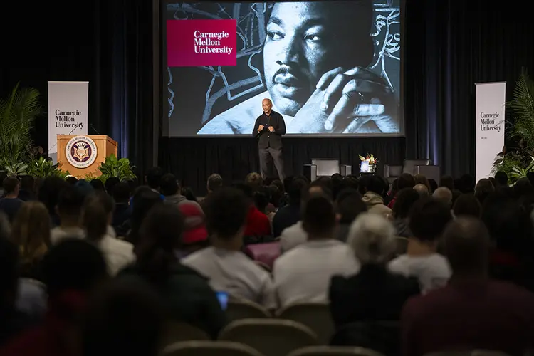 Byron Pitts on stage in front of crowd with MLK image on big screen behind him