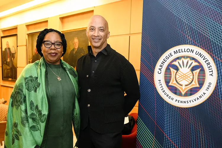 Wanda Heading-Grant standing with Byron Pitts next to CMU seal on Tartan plaid bannerd