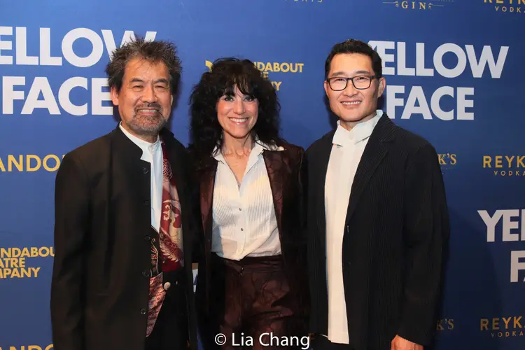 A woman stands between two men in front of a backdrop that reads "Yellow Face" on the left and right