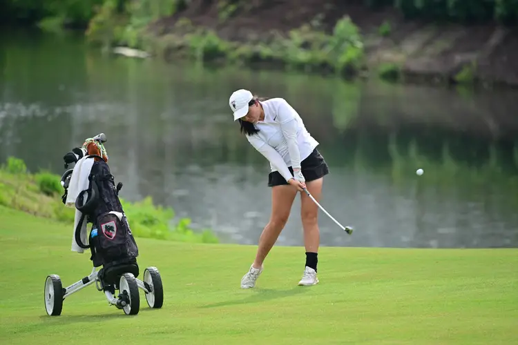 A golfer hits a ball next to a lake.