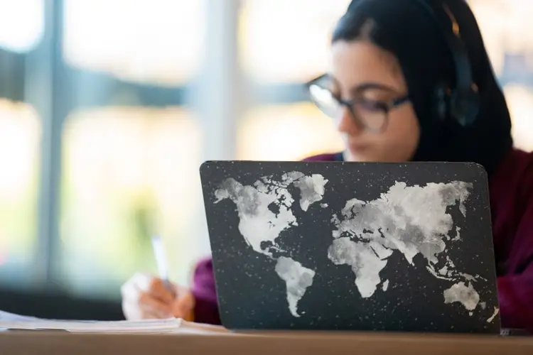 A student sits behind a laptop, using a pen