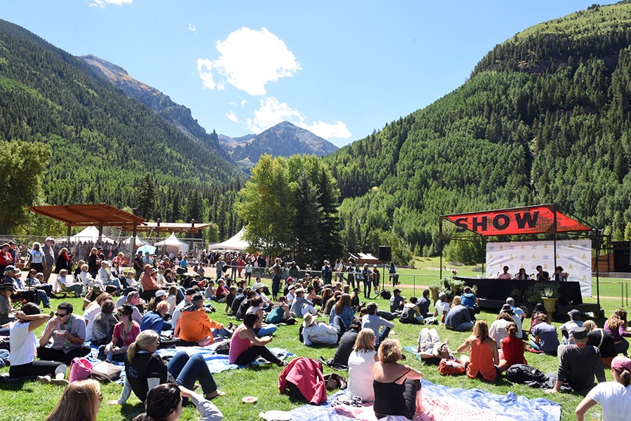 Image of picnic participants sitting in a meadow with mountains in the background