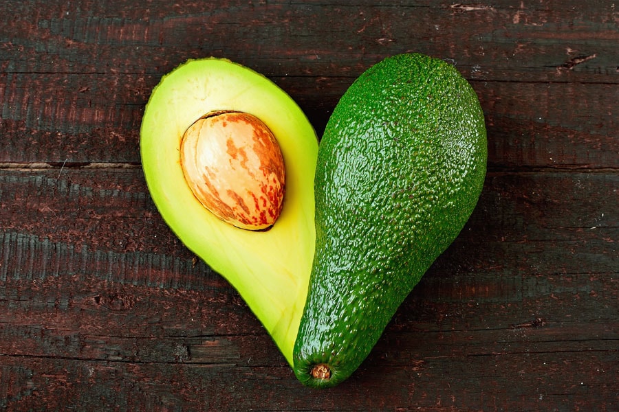 Premium Photo  Avocado cut in half on a wooden table, coriander and basil  next to a straw bag. concept of proper and healthy nutrition, vegetarianism.