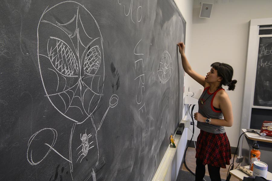 Photo of Izzy Sio drawing on a chalkboard.