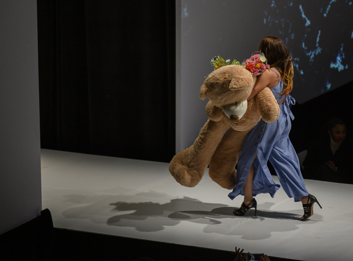 A designer leave the stage with a large teddy bear.