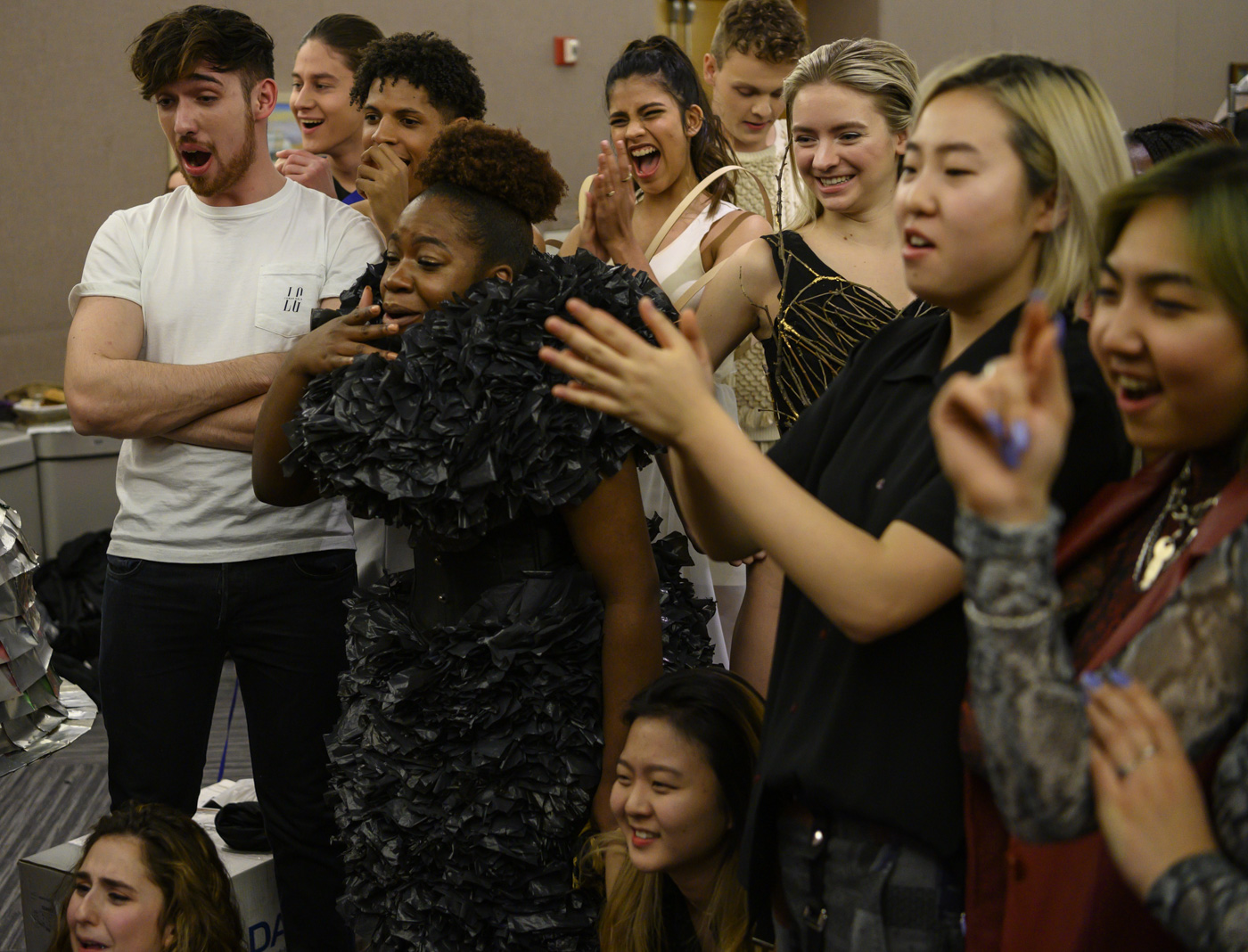 Backstage, models watch the show and cheer on a tv.