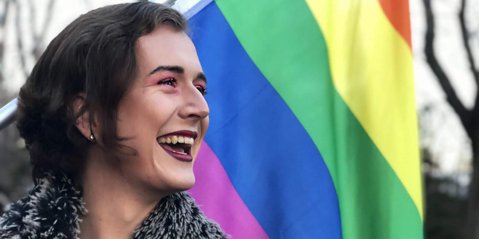 image of student standing in front of a rainbow flag