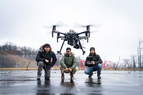three students flying a drone outside