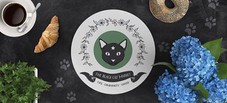 Black Cat Market logo on a dark table with a croissant and blue hydrangea flowers