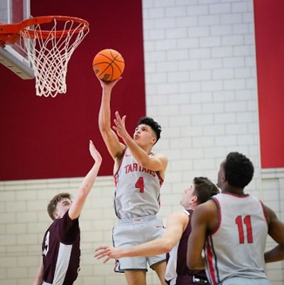 Image of four basketball players, one jumping up to make a shot and another reaching to block the shot