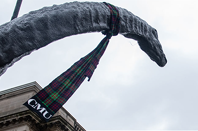 Image of a bronze dinasour status, known as Dippy the Dinosaur, with a CMU tartan scarf around its neck