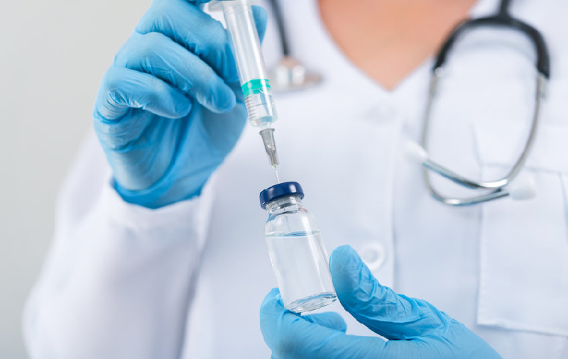 doctor in white coat wearing blue gloves with a syringe and vial