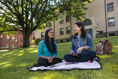 Two students sitting in the grass laughing and smiling
