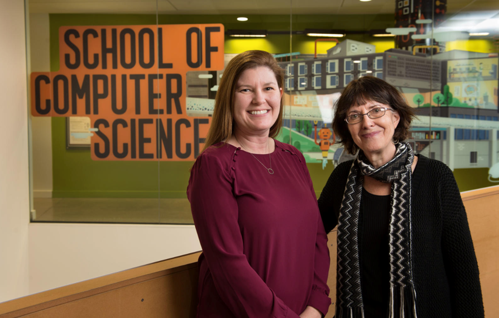 Two women in front of a school of computer sciences sign