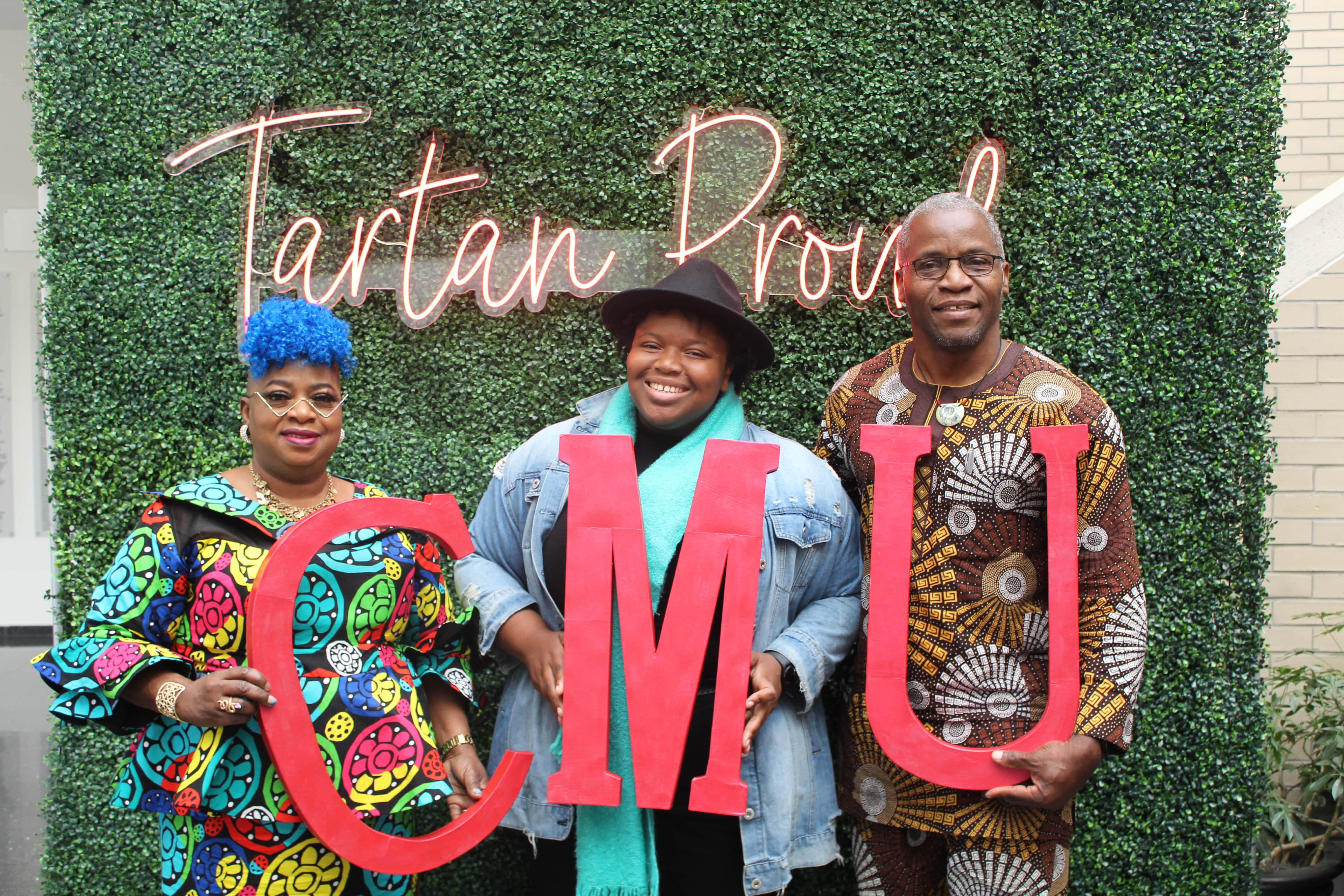 a group of CMU family members standing in front of a Tartan Proud sign