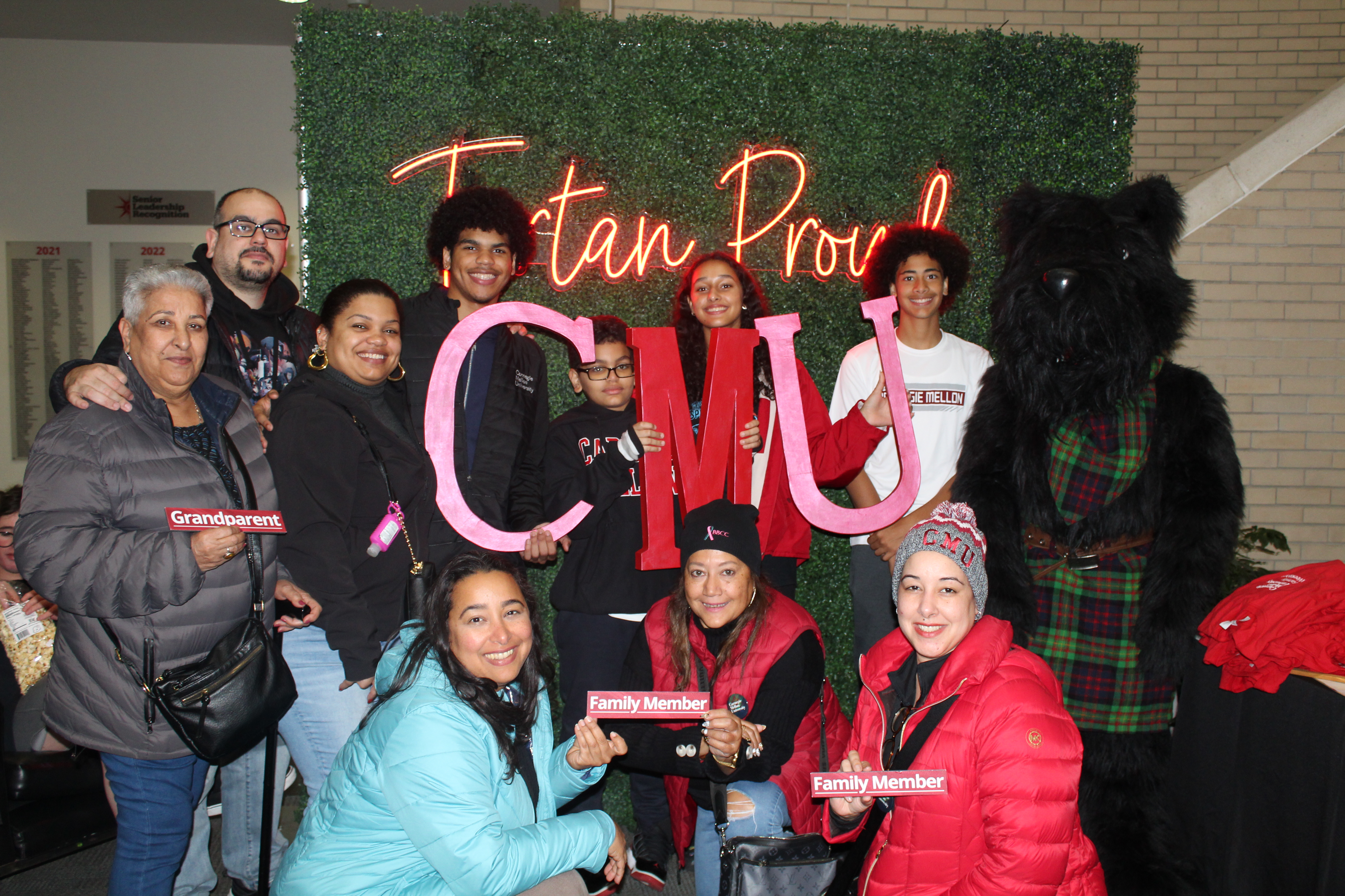 a group of CMU family members standing in front of a Tartan Proud sign